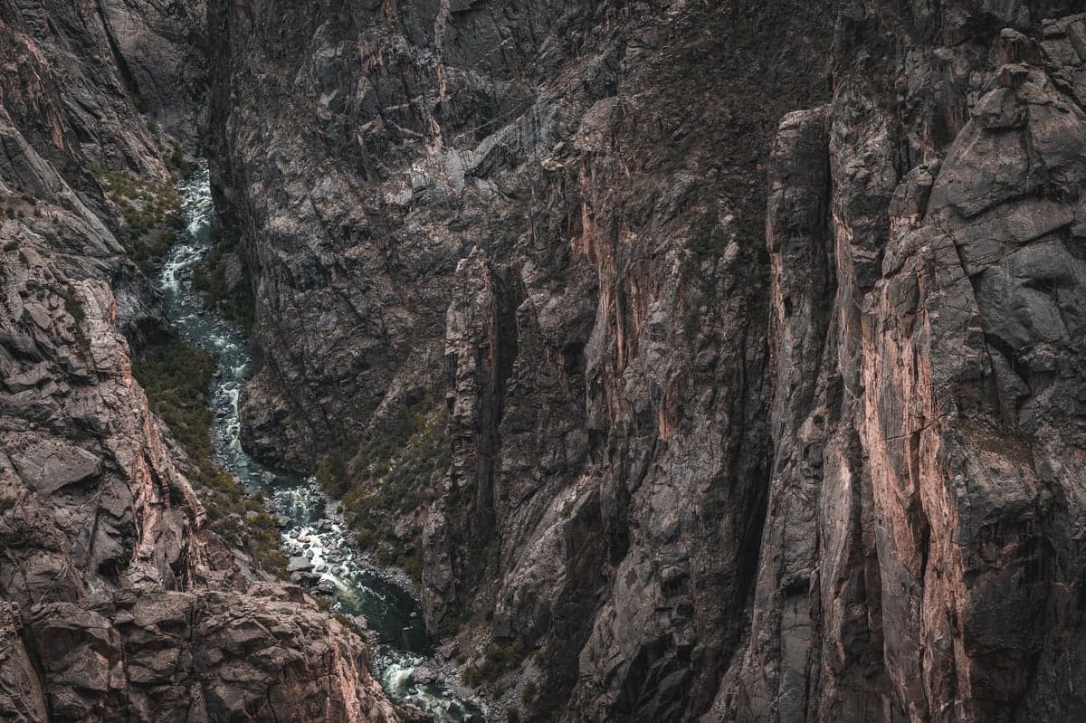 The dark Precambrian walls of Black Canyon rise over 2,000 feet above the Gunnison River. Sunlight reaches the canyon floor only a few hours per day in the narrowest sections.