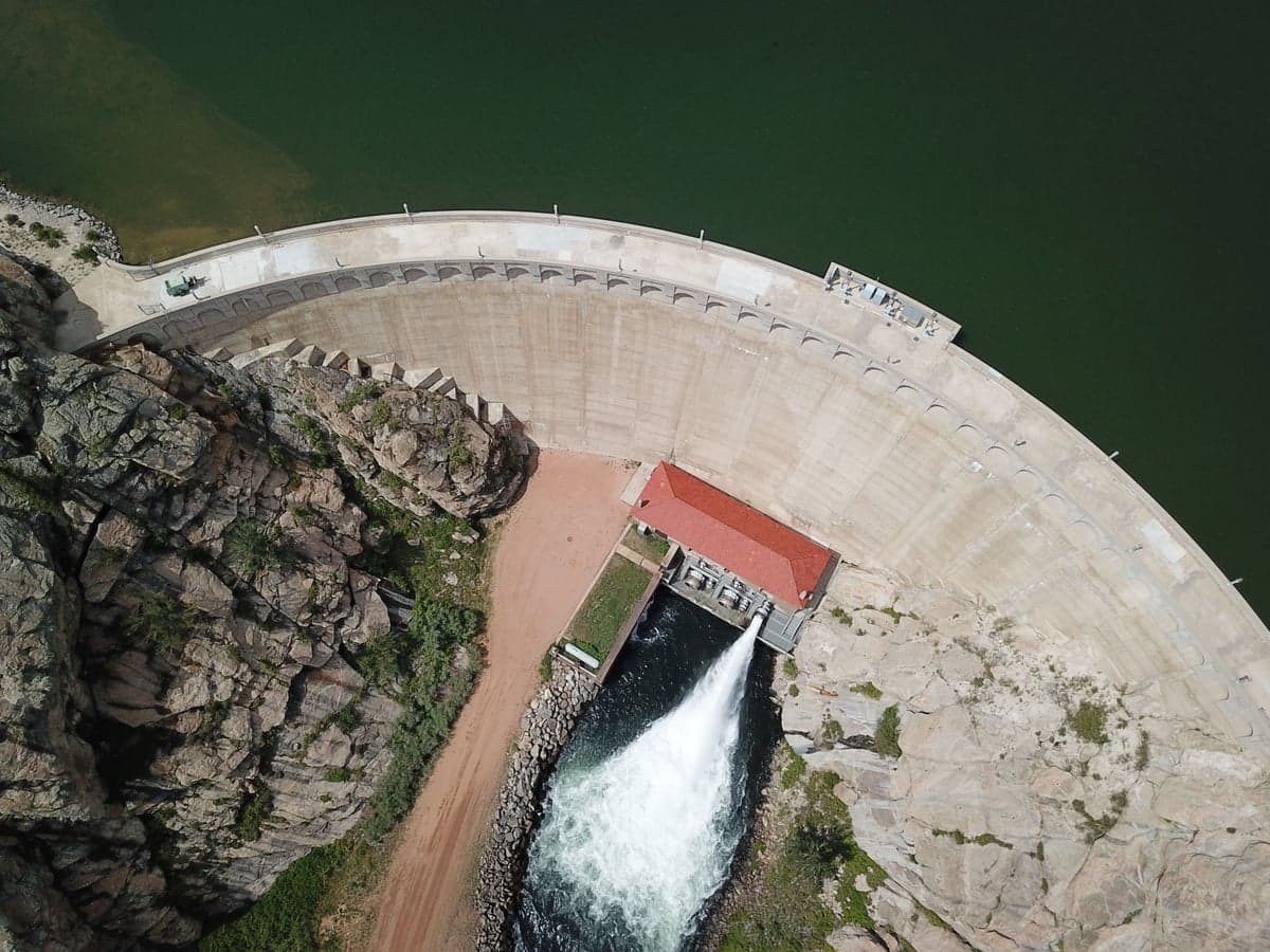 A concrete arch dam releasing water into the canyon below it. Eleven Mile Dam stands 135 feet and draws from near the surface, which is why the canyon warms faster in late summer than a deep bottom-release tailwater.
