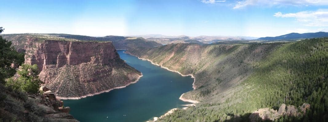 Flaming Gorge from the rim: red rock walls drop into emerald water, with pine-covered slopes stretching toward the Uinta Mountains