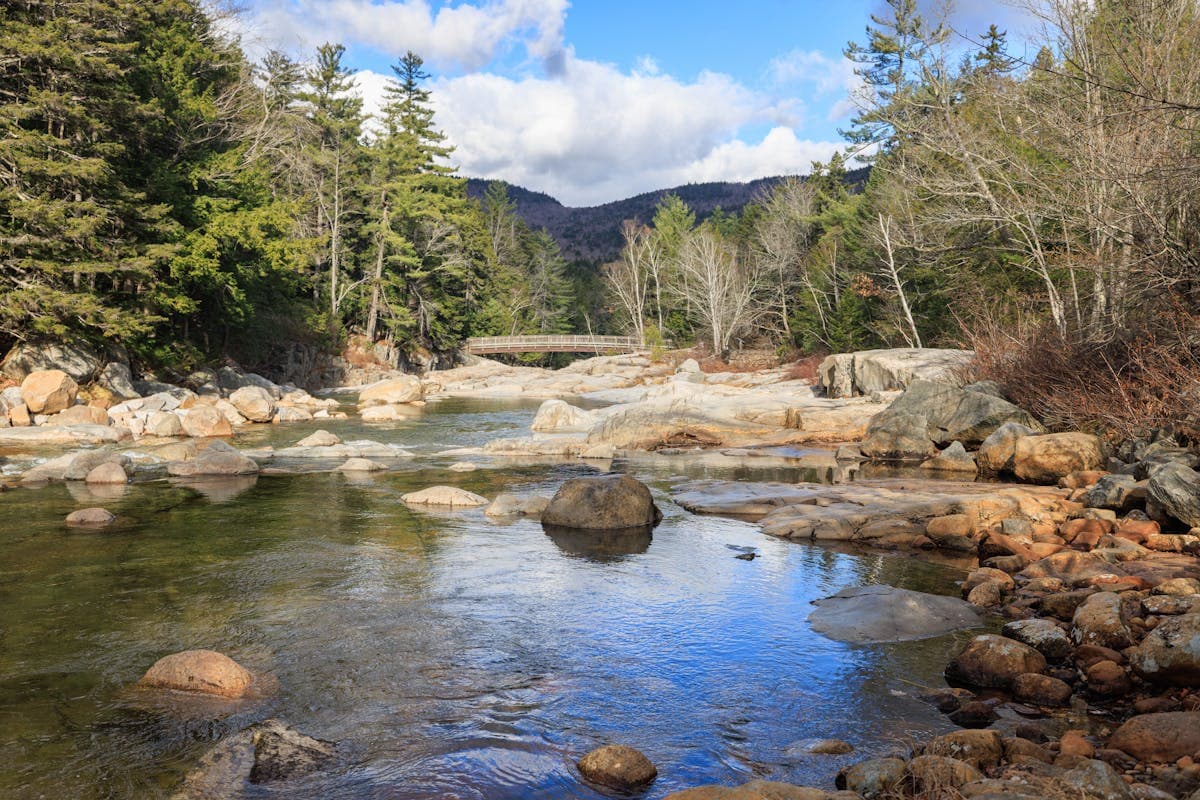Rocky river flowing through dense forest in Albany, New Hampshire with boulders and clear mountain water